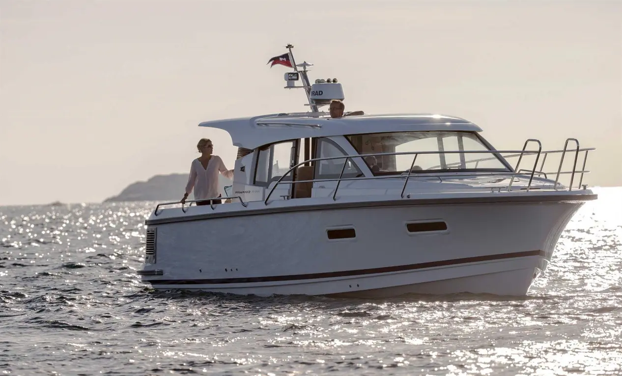 A couple enjoy a sunny day on a luxurious white motorboat, gliding across shimmering water, with distant land visible.